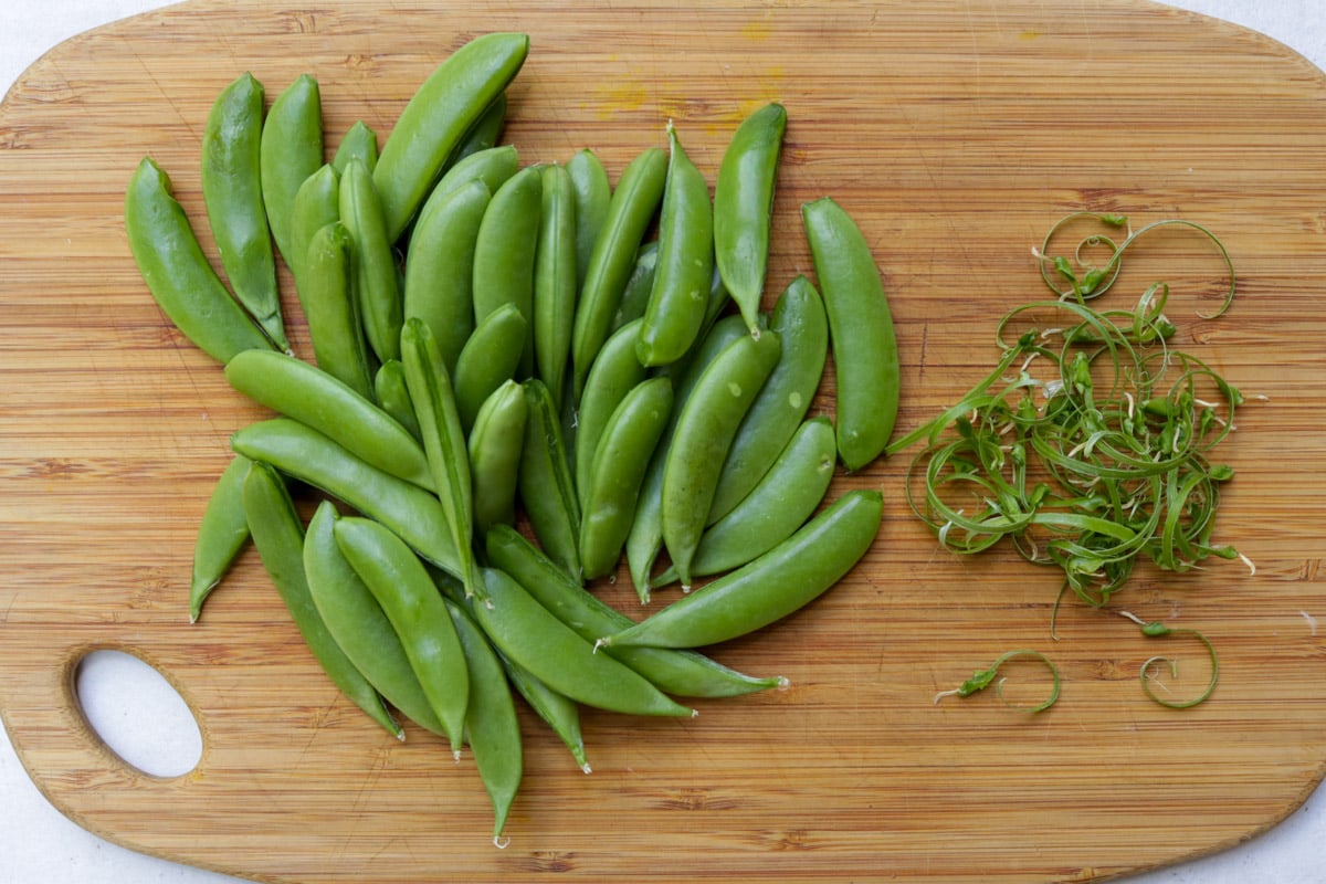 Cleaned bunch of peas and their strings on a cutting board.