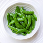 Buttered sugar snap peas in a white bowl.