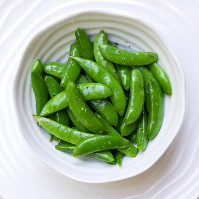 Buttered sugar snap peas in a white bowl.