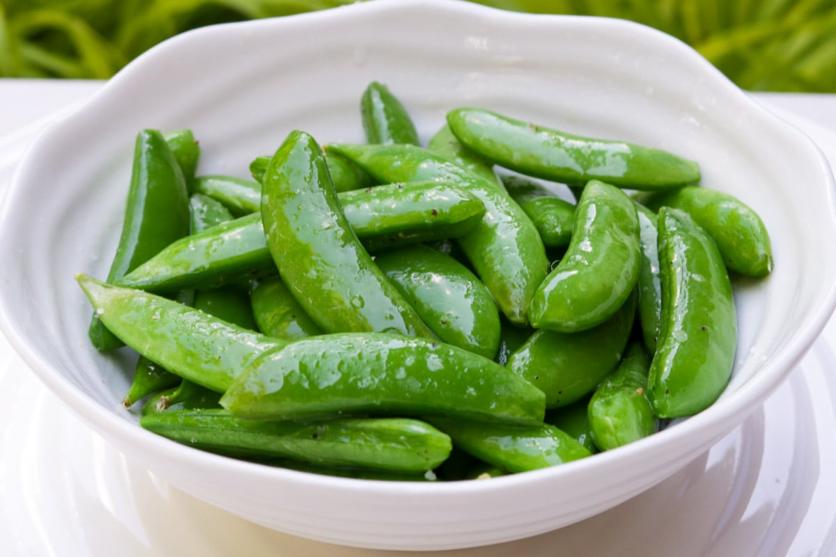 Buttered sugar snap peas in a white bowl.