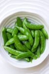 Buttered sugar snap peas in a white bowl.