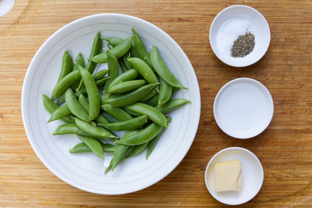 Sugar snap peas, butter, water, salt & pepper on a cutting board. 