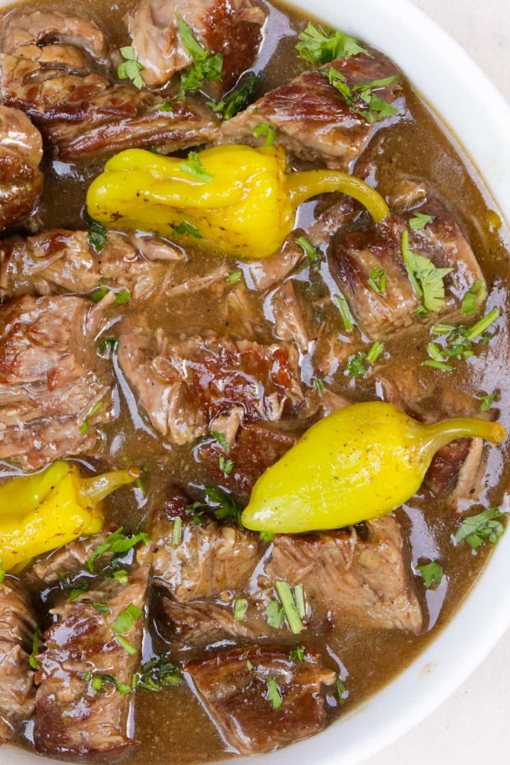 Mississippi pot roast in gravy topped with peppers in a white bowl.