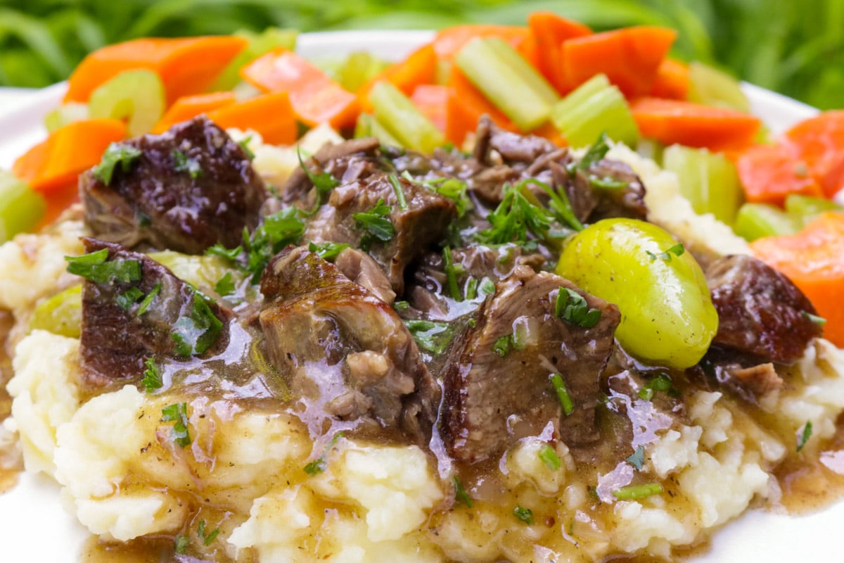 Mississippi pot roast with gravy over mashed potatoes beside a carrot and celery medley.