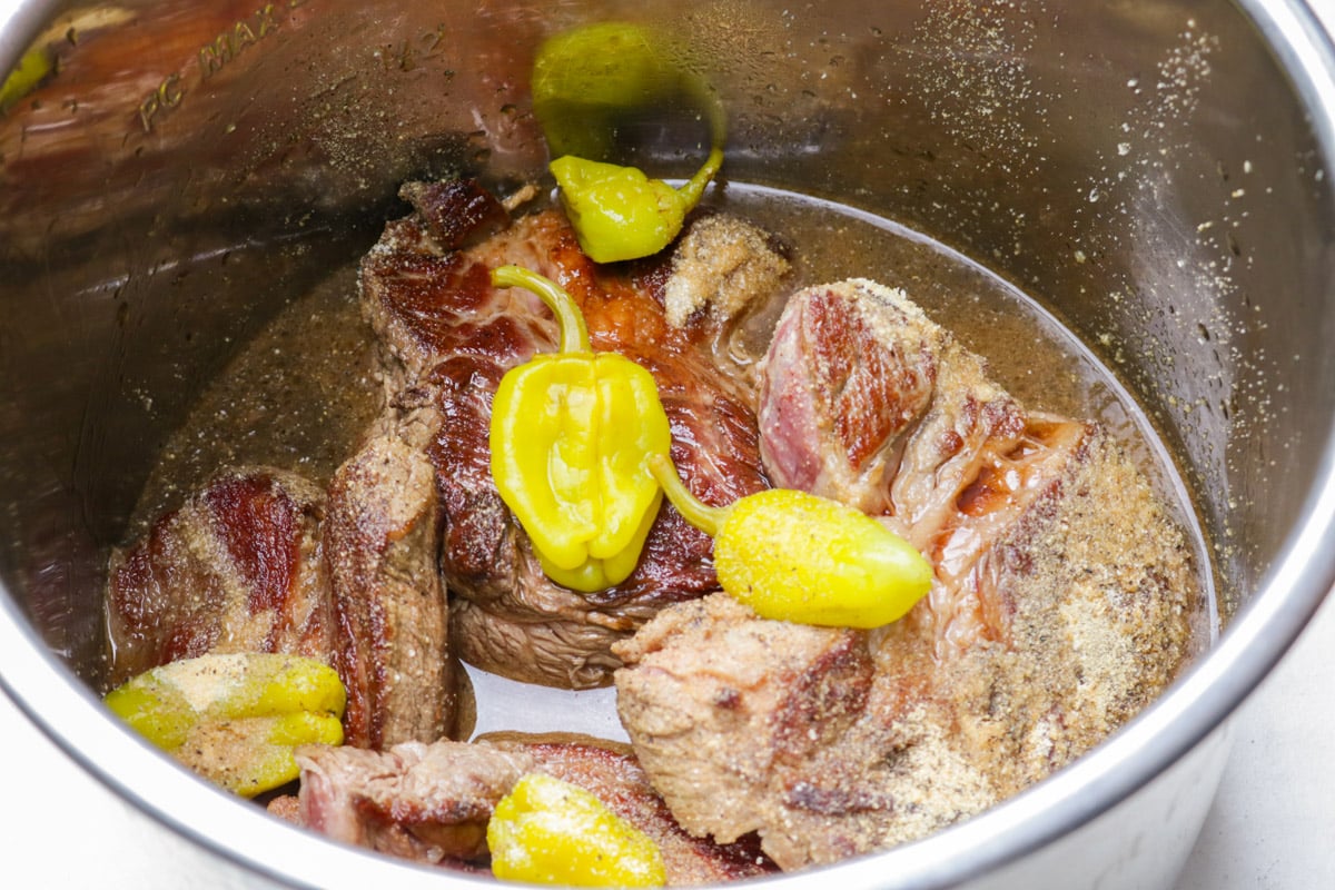 Seared chuck in Instant pot topped with broth, seasonings and pepperoncini peppers.
