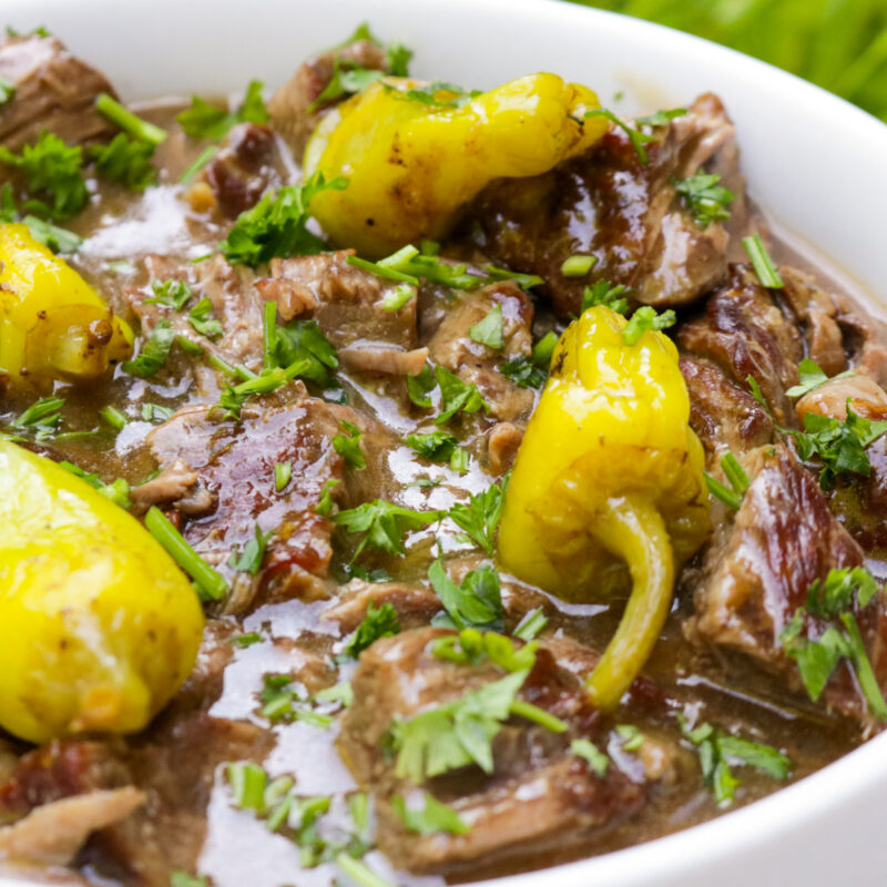 Mississippi pot roast in gravy topped with pepperoncini peppers n a white bowl.