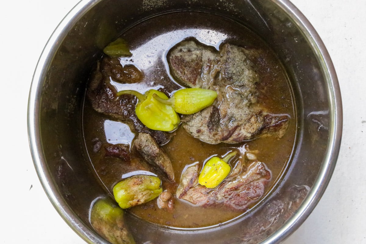 Mississippi pot roast in beef liquid in an Instant Pot with yellow peppers.