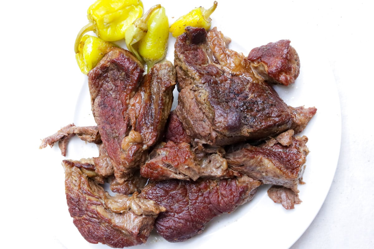 Cooked beef chuck on a plate with yellow peppers.