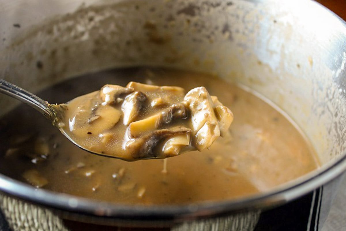 Spoon of mushroom gravy over the pot of gravy.