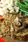 Two slices meatloaf with mushroom gravy, mashed potatoes and green beans on red plate.