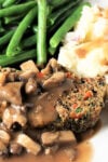 Two slices meatloaf with mushroom gravy, mashed potatoes and green beans on red plate.