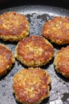 Six salmon patties frying in skillet.