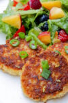 Three salmon patties and salad on a plate.