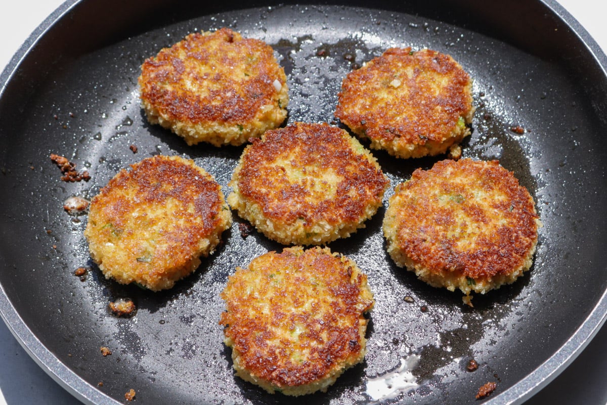 6 salmon patties frying in skillet, second golden brown side up.