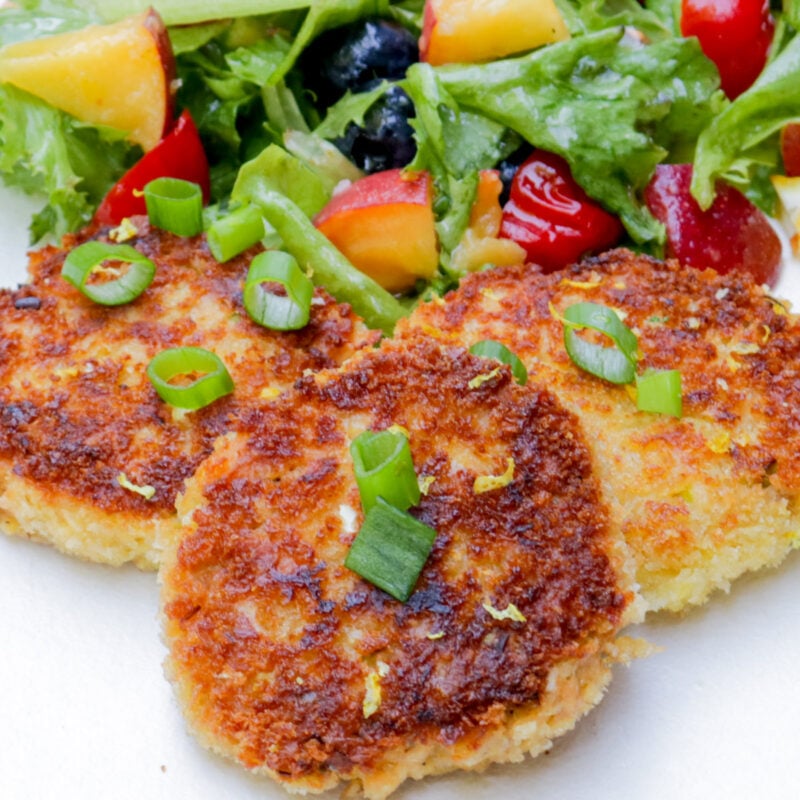 Three salmon patties and salad on a plate.