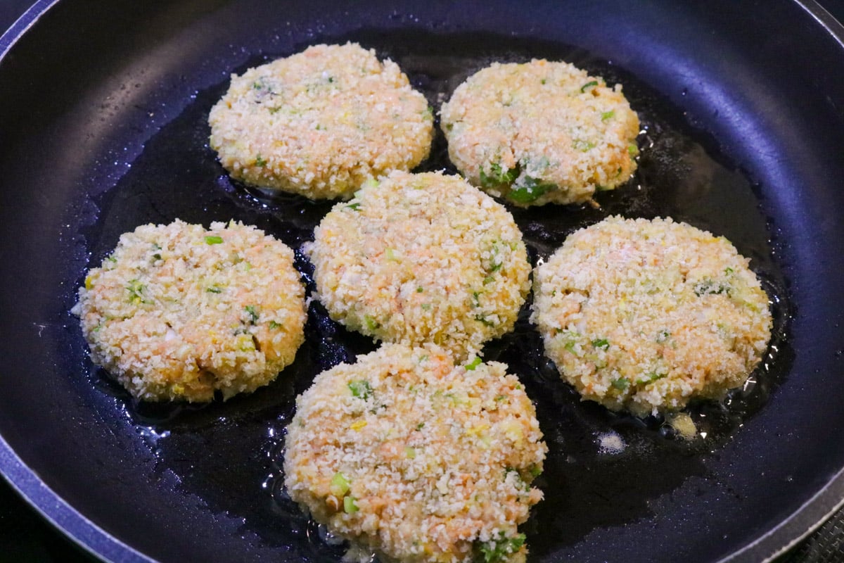 6 salmon patties frying in skillet, first side.