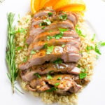 Sliced turkey thighs over quinoa with sauce on top garnished with orange slices.