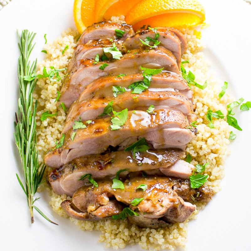 Sliced turkey thighs over quinoa with sauce on top garnished with orange slices.