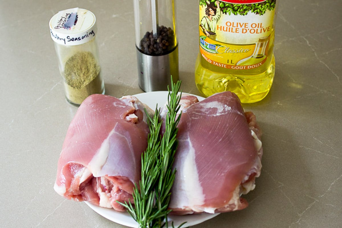 Two raw boneless turkey thighs, fresh rosemary sprig, poultry seasoning, pepper, oil.