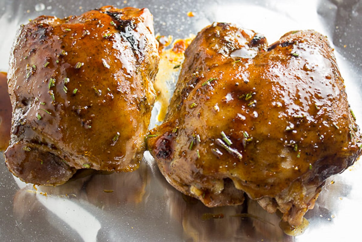 Two cooked glazed boneless turkey thighs on foil lined pan.