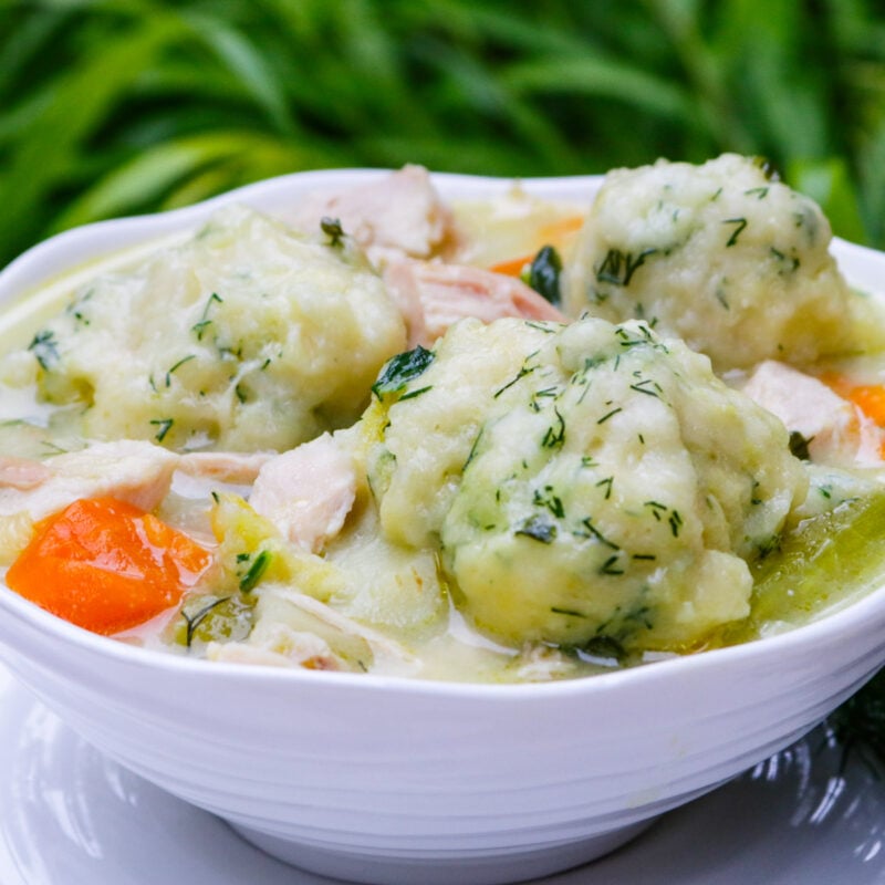 Chicken and dumpling soup in a bowl with a plate underneath.