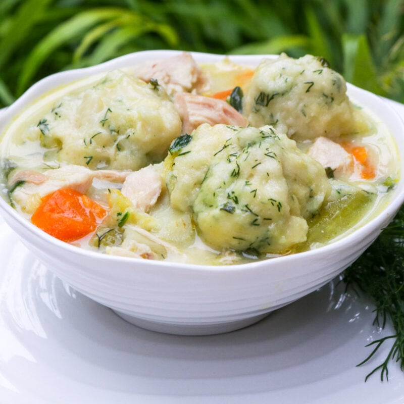 Chicken and dumpling soup in a bowl with a plate underneath.