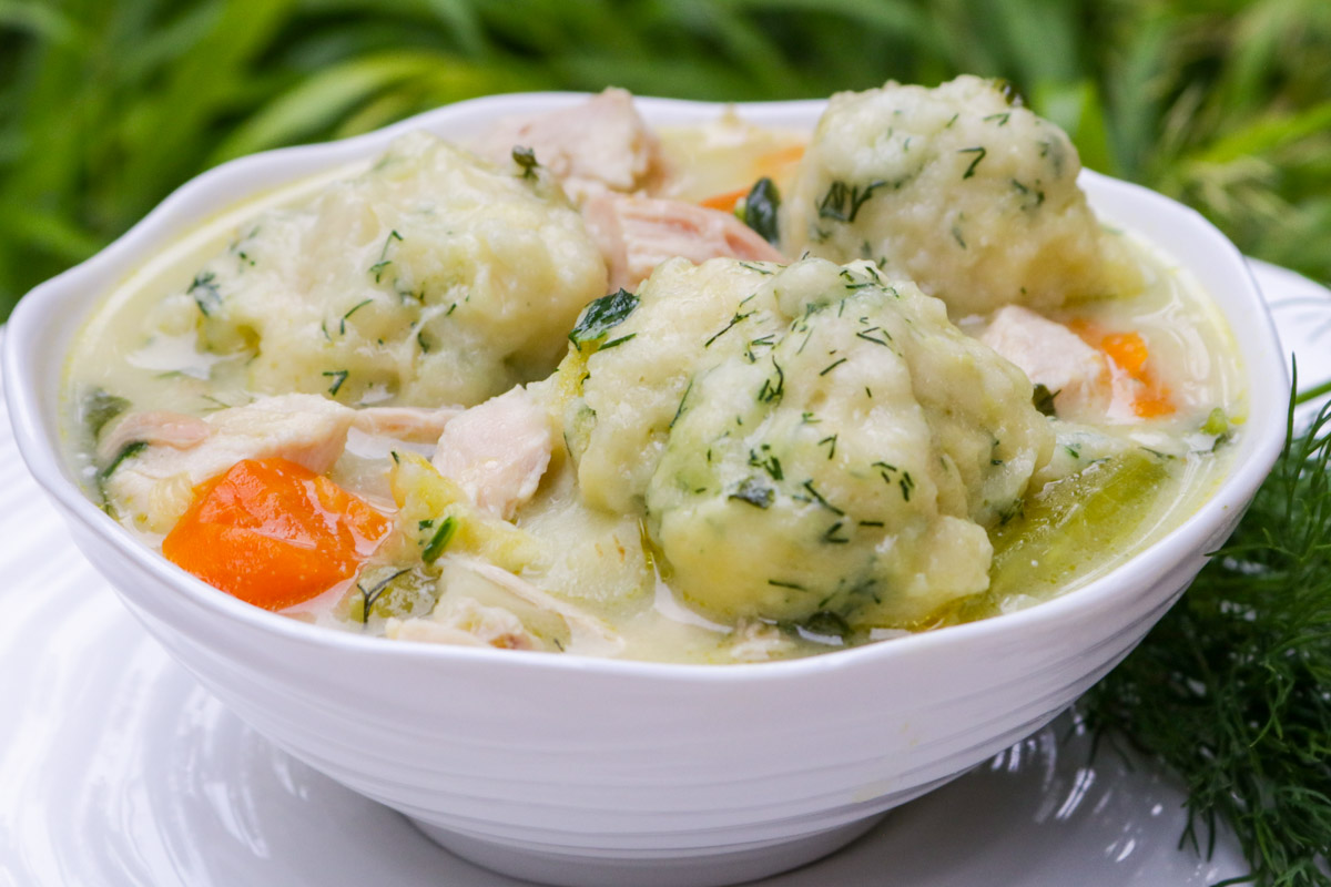 Chicken and dumpling soup in a bowl with a plate underneath.