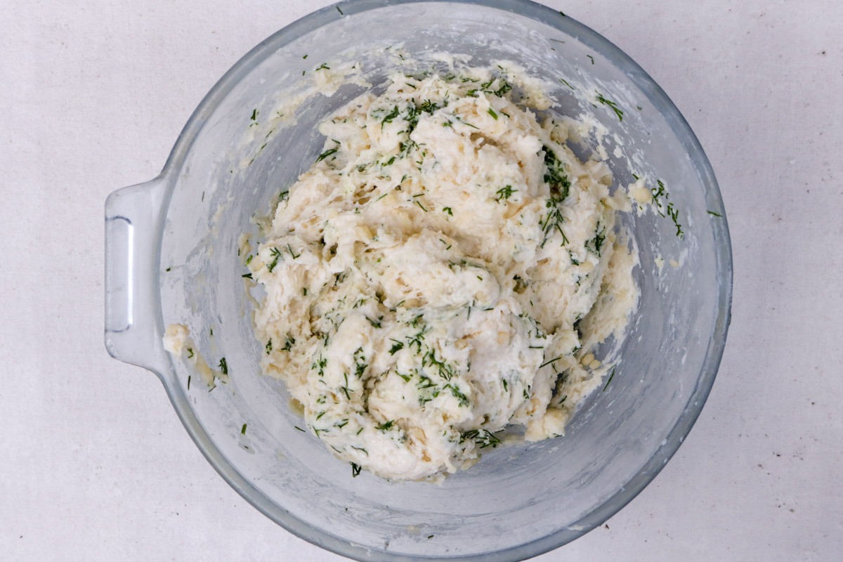 Large ball of dumpling dough with dill in a bowl.